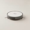 Robot aspirateur compact rond vu de trois quarts sur fond gris clair Robot aspirateur compact rond vu de trois quarts sur fond gris clair